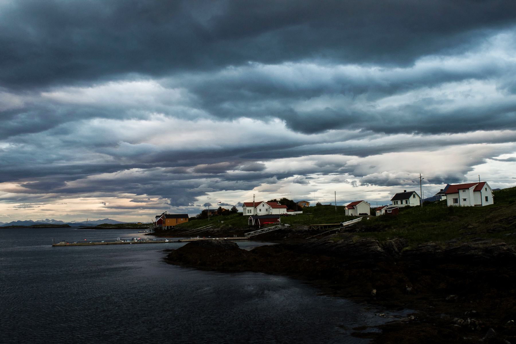 White and red houses along the shore of Fleinvær under heavy cloud
