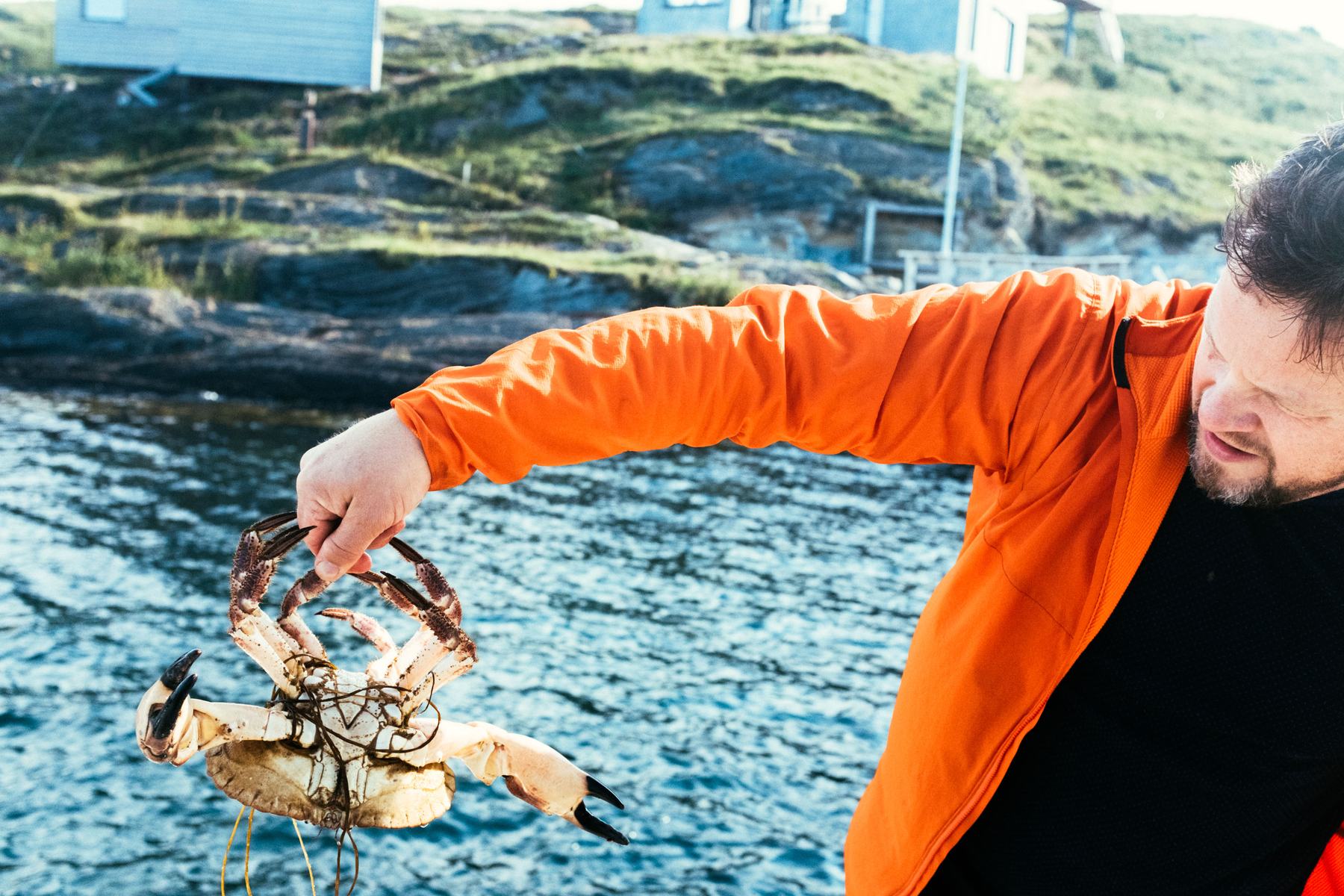 A man in an orange jacket holding up a crab by the harbour