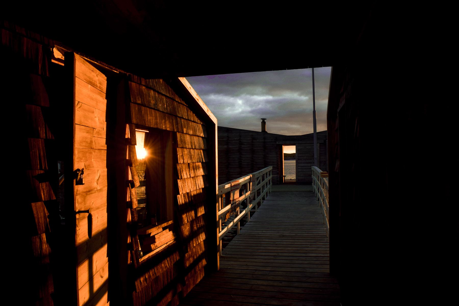 Lamplight on a dark timber wall and the boardwalk at dusk