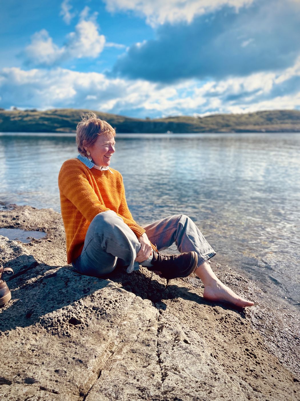 Megan sitting on a sunlit rock by the sea