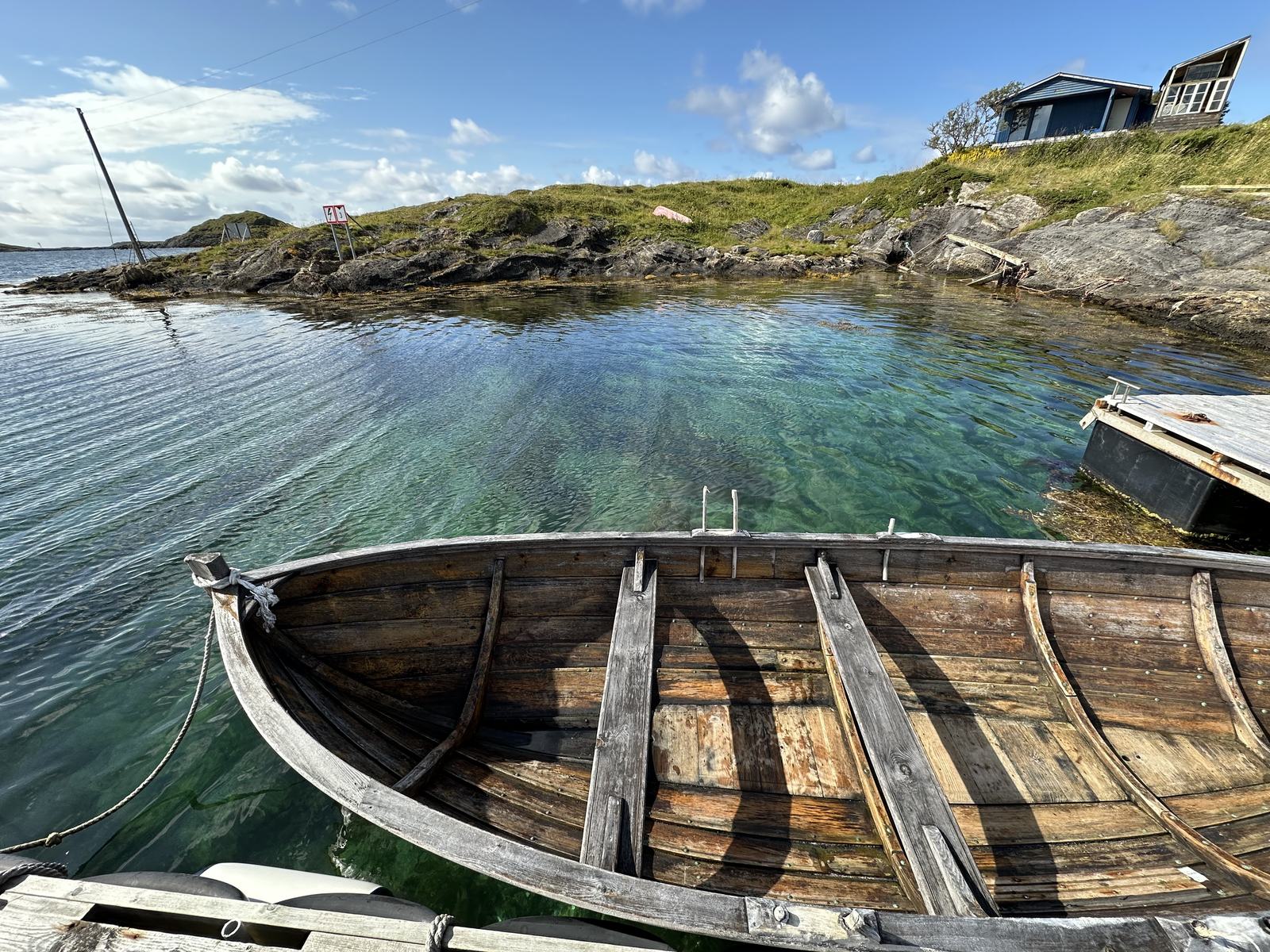 A wooden rowing boat in clear, shallow water by the shore