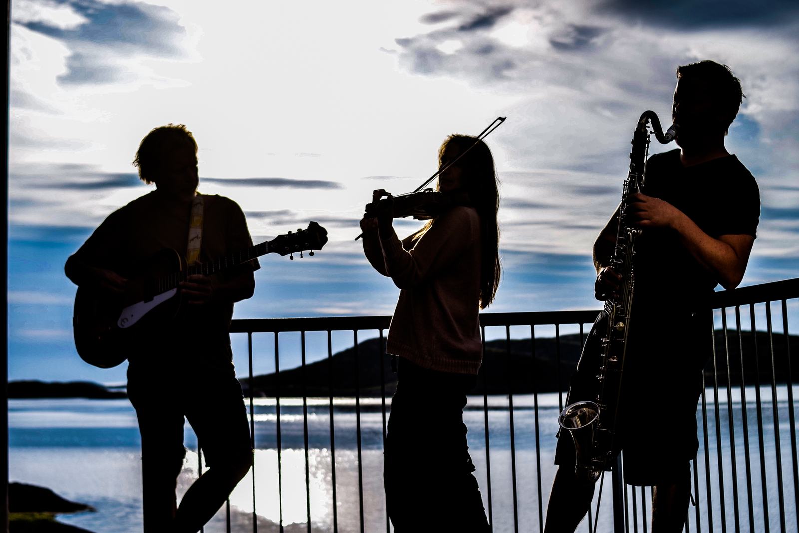 Three musicians playing on the balcony, silhouetted against the sea