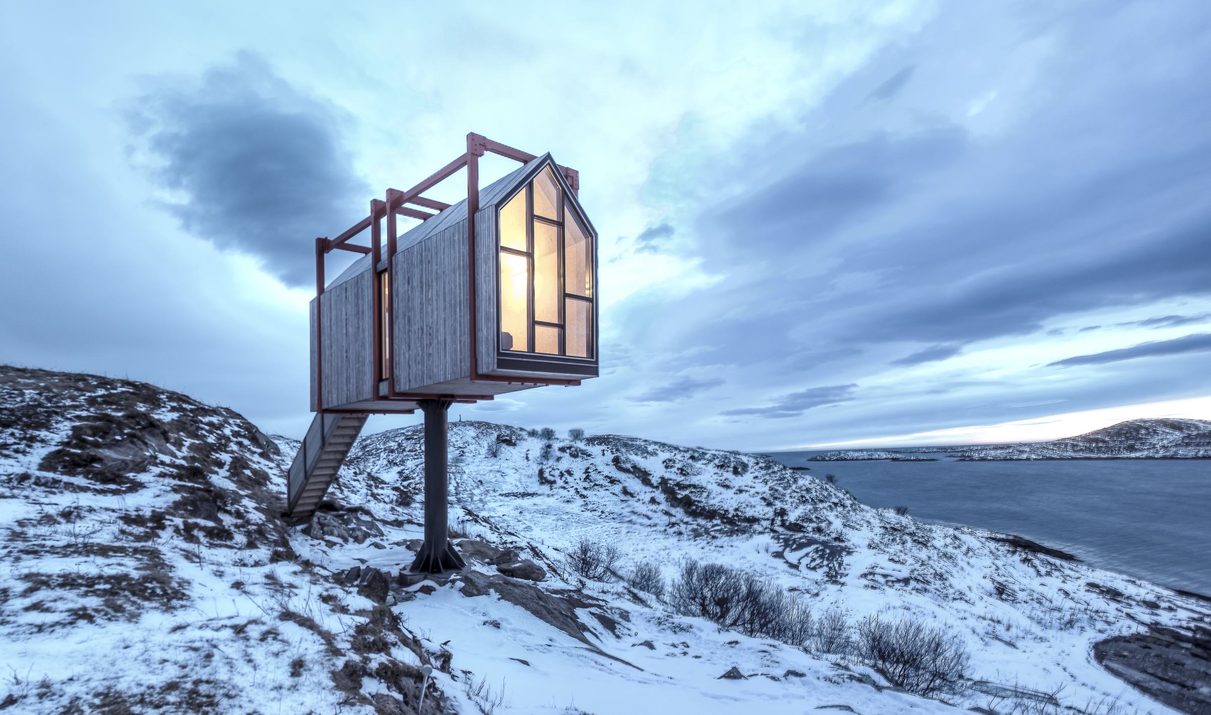 Njalla, the raised Tower House, in snow at dusk, windows lit, sea behind