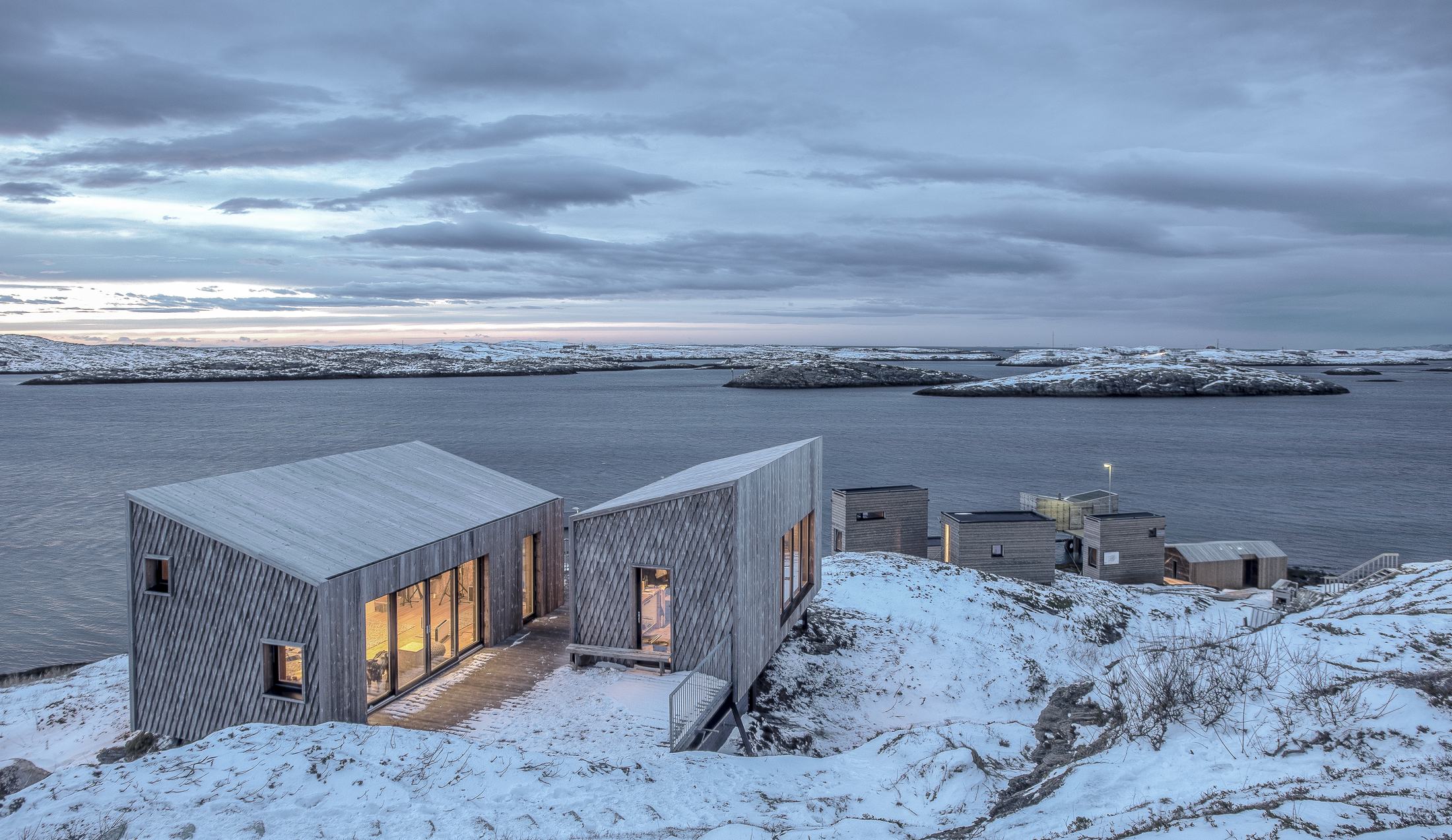 Two timber tiny houses on snowy rock above the sea and scattered islands