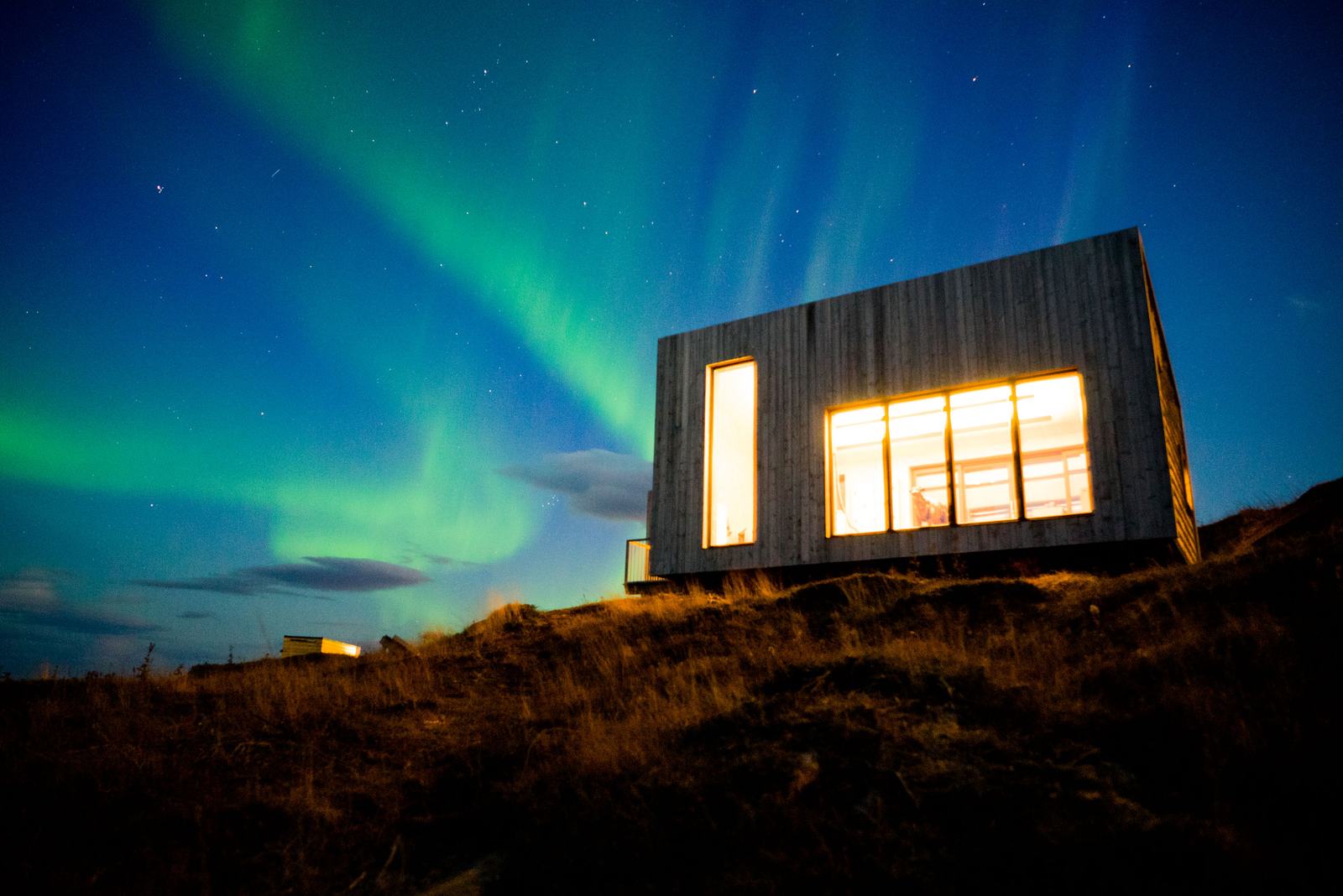 Northern lights over a lit cabin on the hill at night