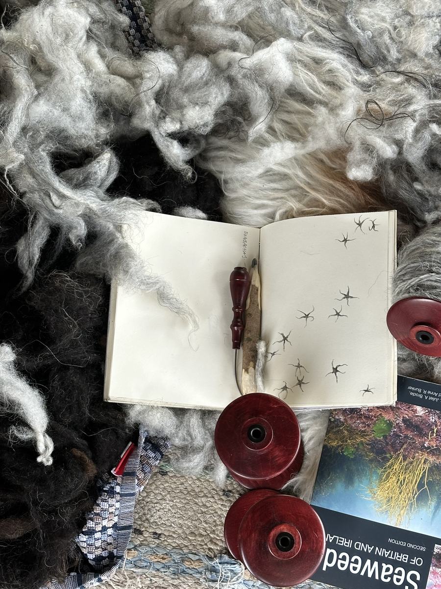 A sketchbook, raw wool and thread on the studio table