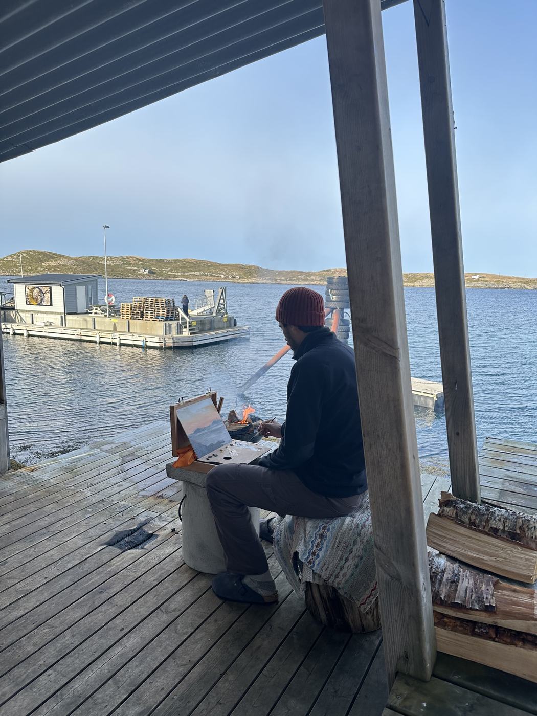 Eduardo painting at an easel in the Crab Trap, the sea behind him