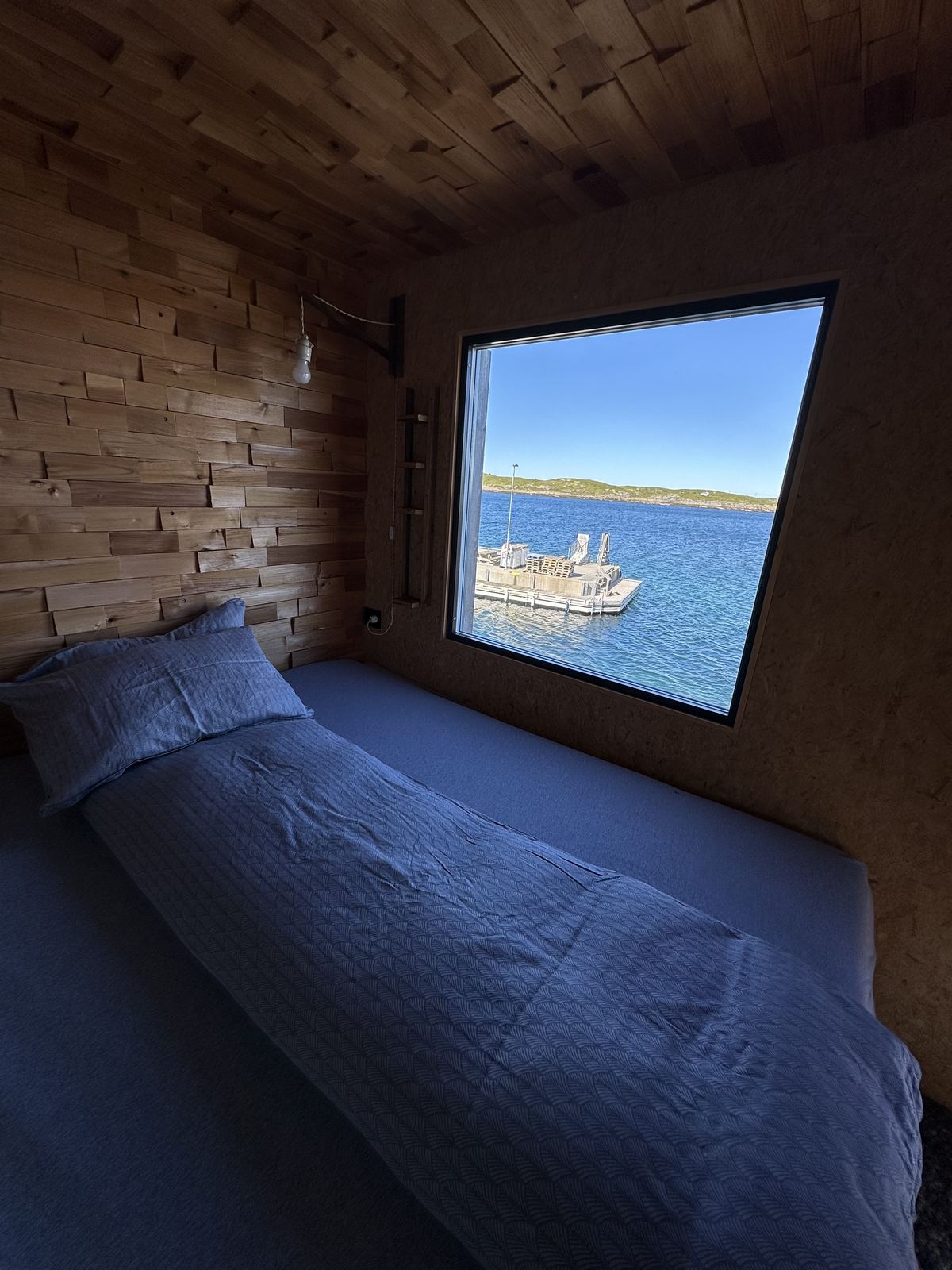 A sleeping cabin: a made bed under a window looking out to the sea