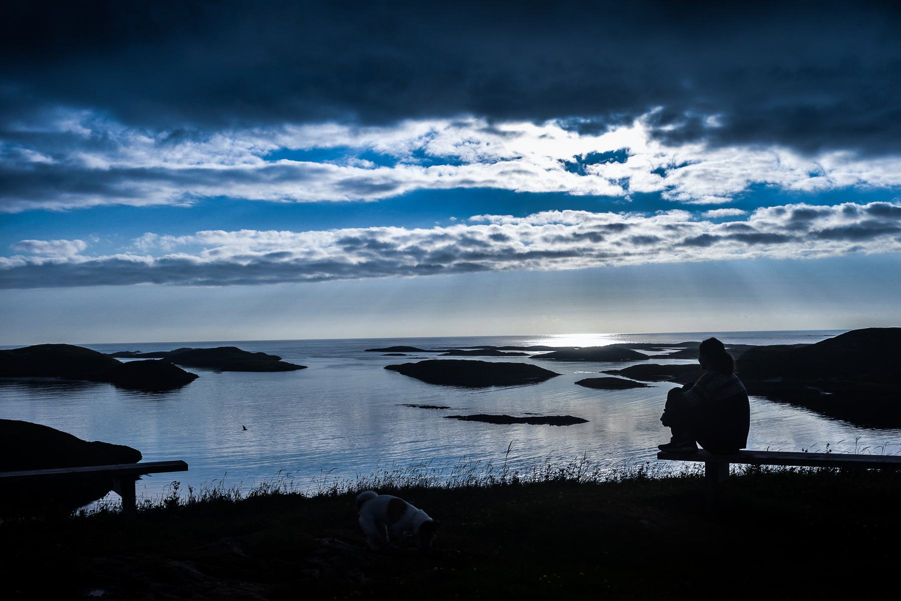 A person sitting on the hill at dusk, looking over the islands