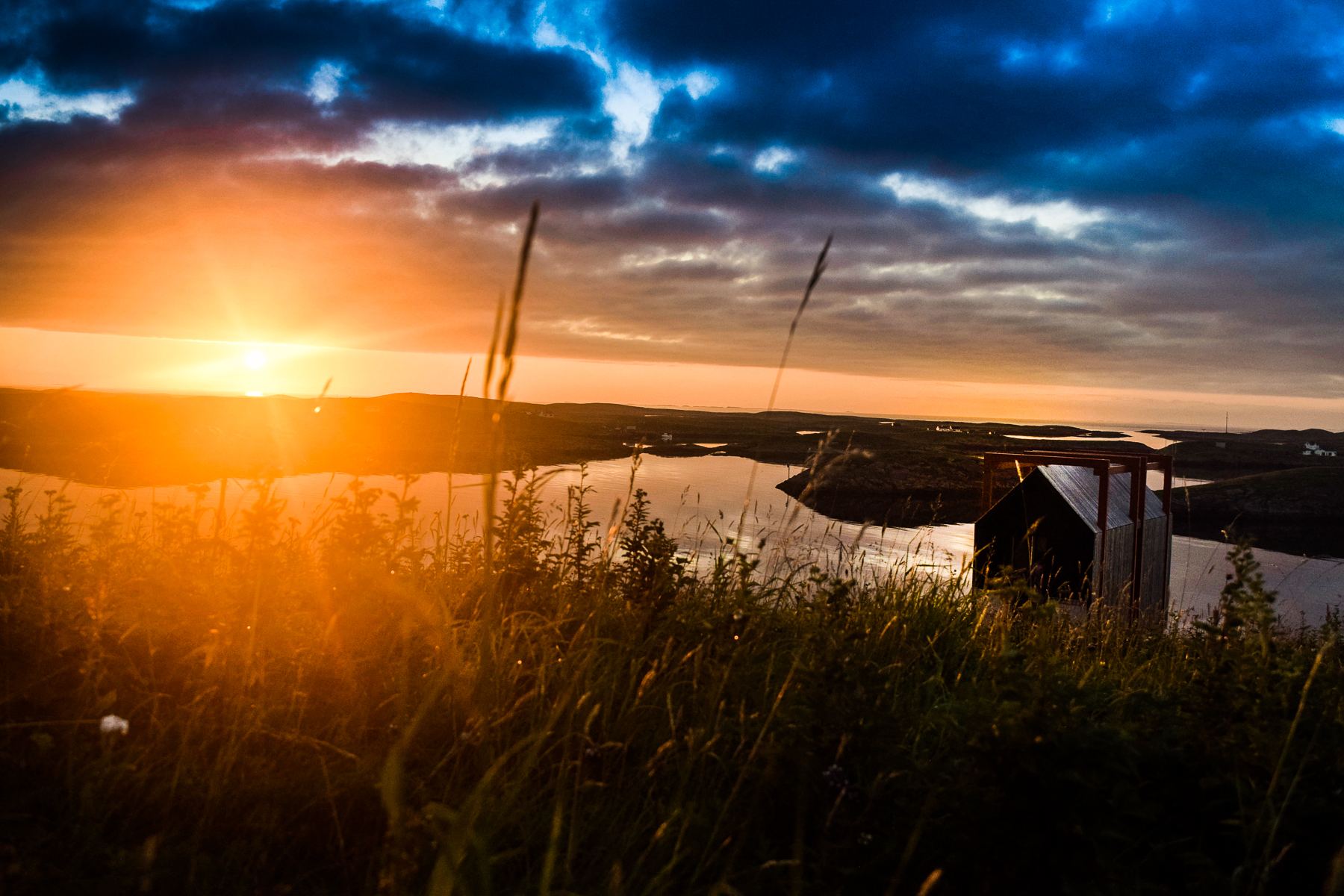 Low sun over the water, a cabin in silhouette on the shore