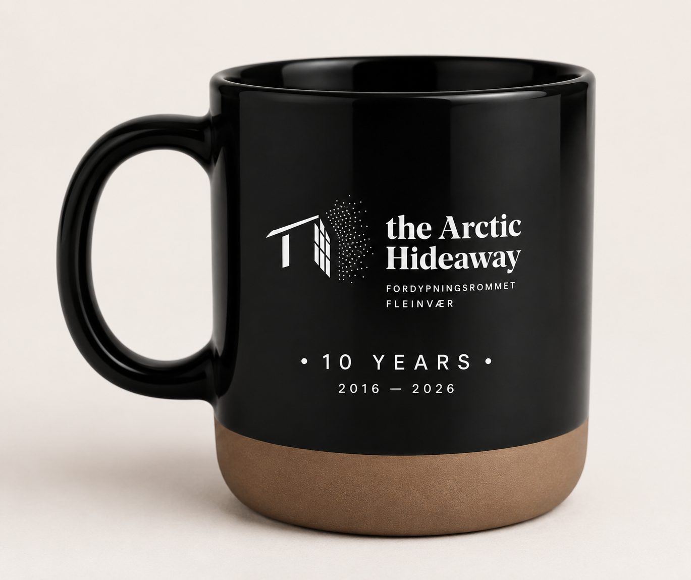 A black mug with The Arctic Hideaway logo and the words 10 Years, 2016–2026, on a clay-coloured base