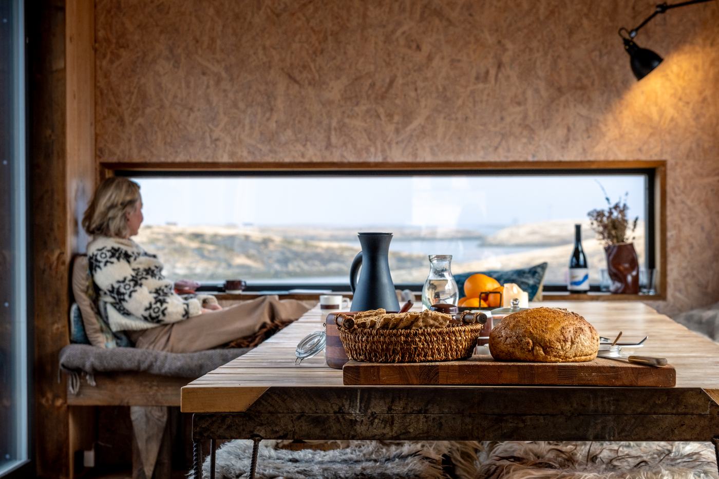A guest by the long window in the Kitchen House, bread and coffee on the table