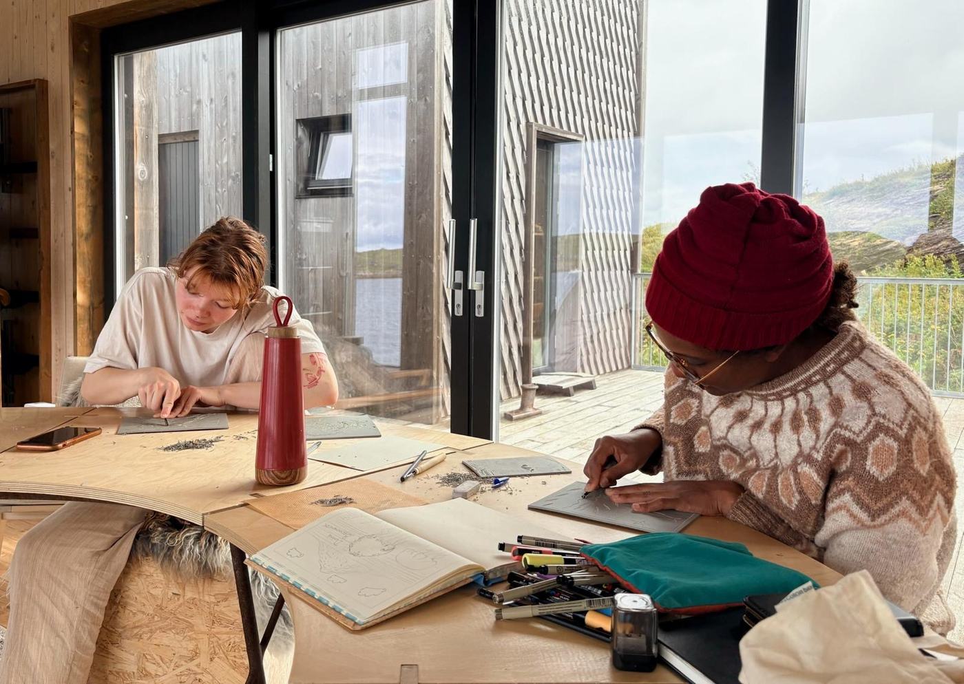 Two artists drawing at a table in the Studio House